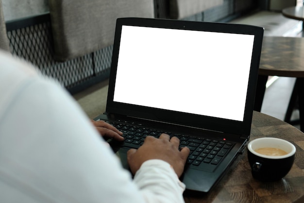 Mockup image of a man using and working on laptop computer with a blank white screen with coffee cup on wooden table in cafe