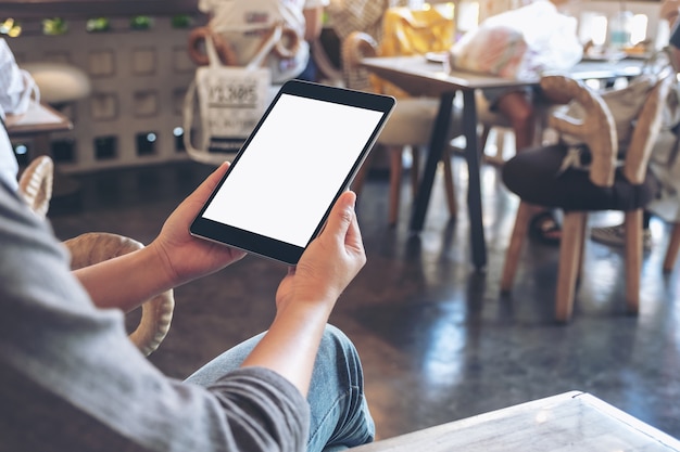 Mockup image of a woman holding black tablet pc with blank white screen while sitting in cafe