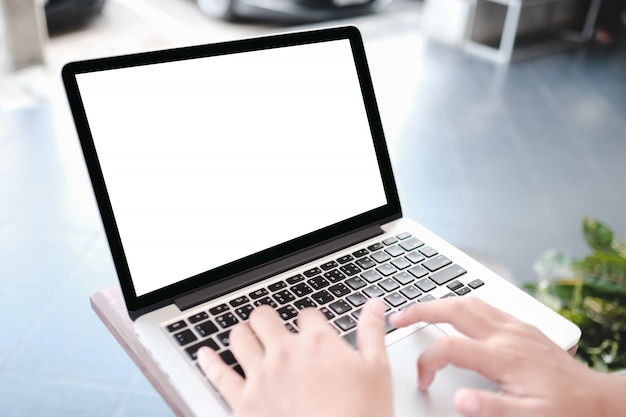 Mockup image of a woman holding blank mobile phone while using laptop with blank  screen on table in cafe.