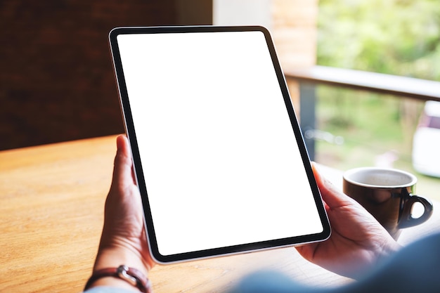 Mockup image of a woman holding digital tablet with blank white desktop screen in cafe