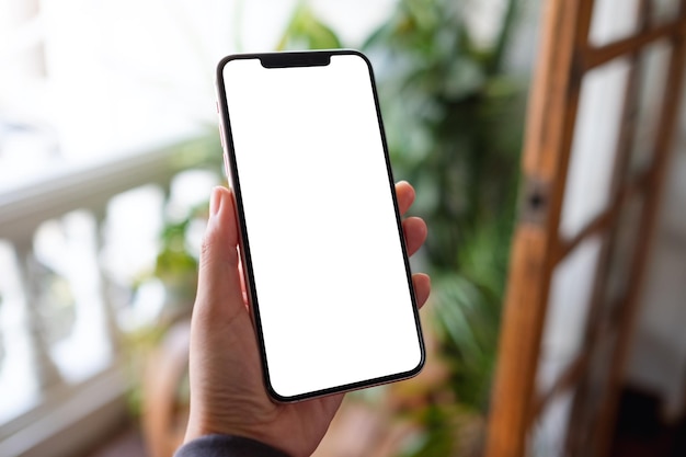 Mockup image of a woman holding mobile phone with blank desktop screen on balcony at home