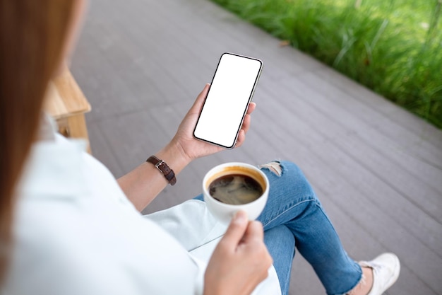 Mockup image of a woman holding mobile phone with blank white desktop screen while drinking coffee in the outdoors