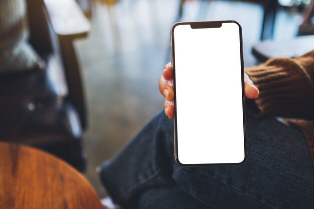 Mockup image of a woman holding and showing black mobile phone with blank screen in cafe