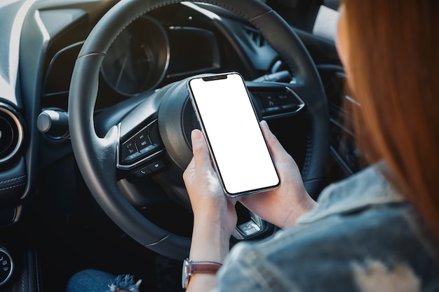 Mockup image of a woman holding and using mobile phone with blank screen while driving car