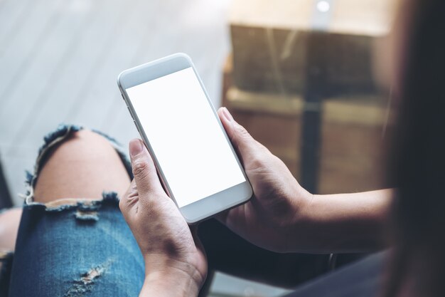 Mockup image of a woman holding white mobile phone with blank screen while sitting in cafe