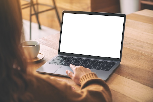 Mockup image of a woman's hand using and touching on laptop touchpad with blank white desktop screen with coffee cup on wooden table