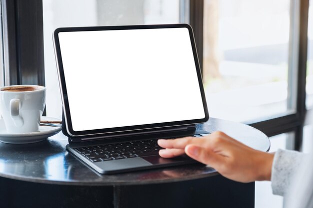 Mockup image of a woman touching on tablet touchpad with blank white desktop screen as a computer pc with coffee cup on the table