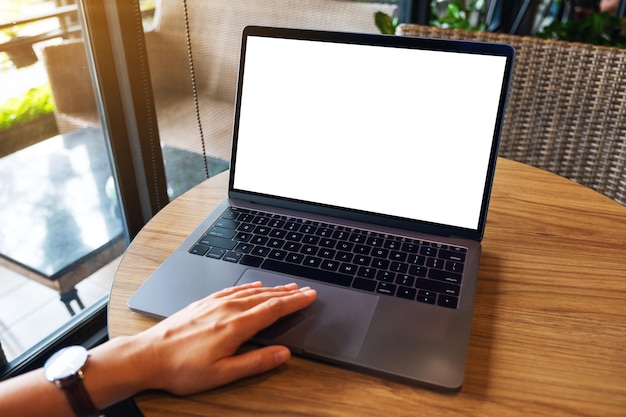 Mockup image of a woman using and touching on laptop computer touchpad with blank white desktop screen on wooden table