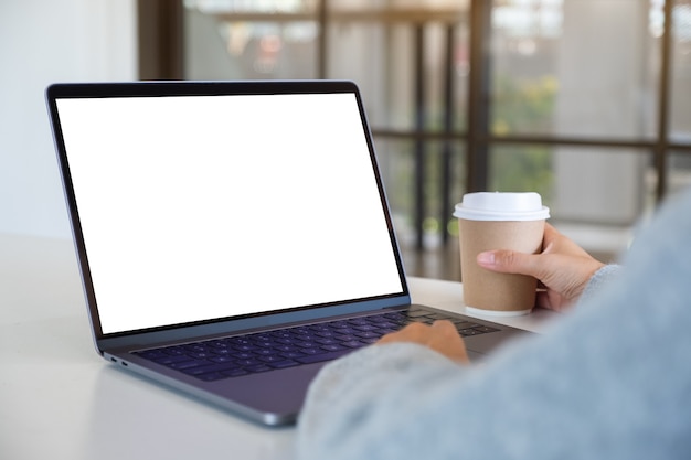 Mockup image of a woman using and touching on laptop touchpad with blank white desktop screen while drinking coffee