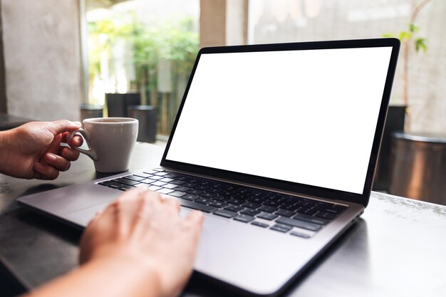 Mockup image of a woman using and touching on laptop touchpad with blank white desktop screen while drinking coffee