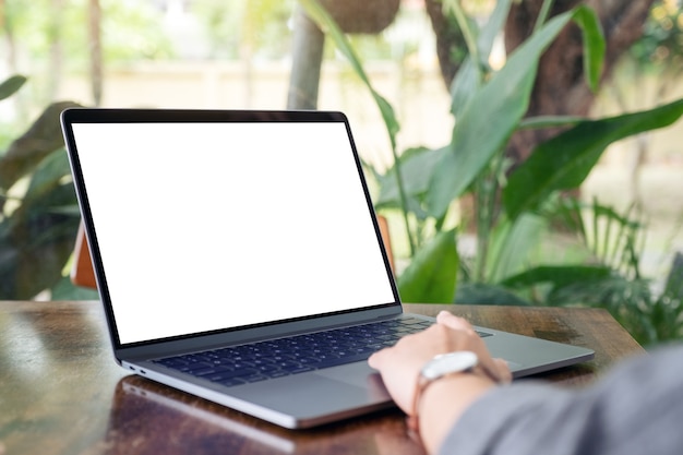 Mockup image of a woman using and touching laptop touchpad with blank white desktop screen on wooden table in cafe