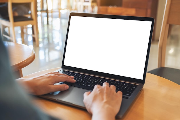 Mockup image of a woman using and typing on laptop computer keyboard with blank white desktop screen on wooden table