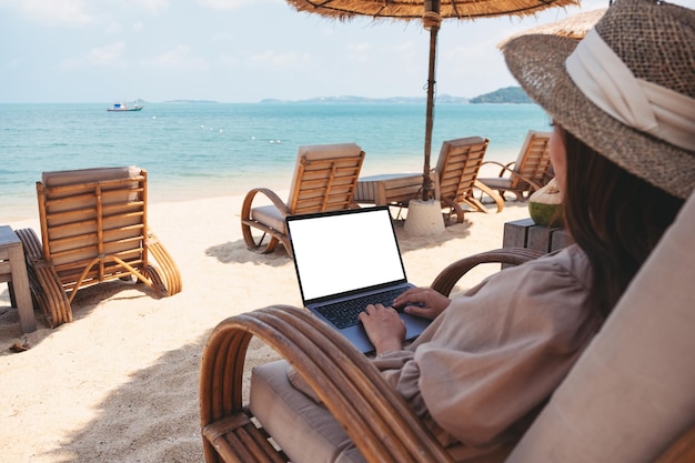 Mockup image of a woman using and typing on laptop computer with blank desktop screen while sitting on the beach