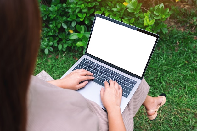 Mockup image of a woman using and typing on laptop with blank white desktop screen in the outdoors