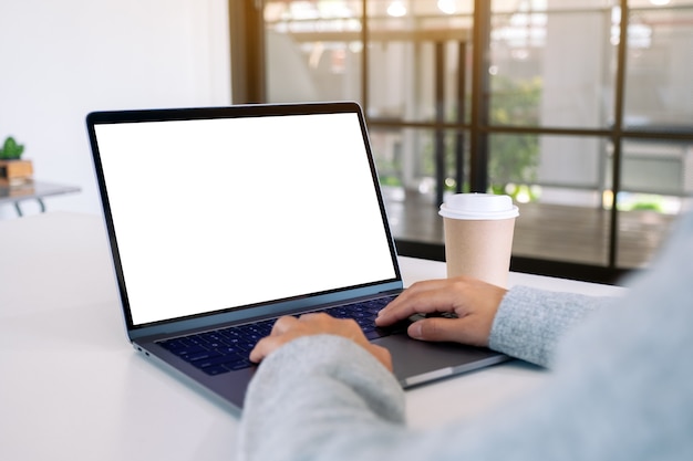 Mockup image of a woman using and typing on laptop with blank white desktop screen with coffee cup on the table