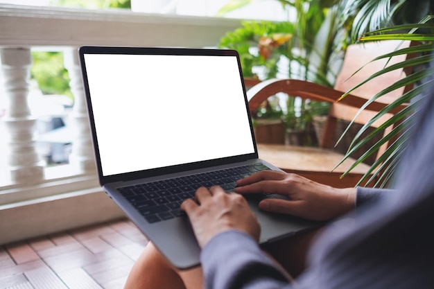 Mockup image of a woman using and working on laptop computer with blank white desktop screen while sitting on balcony at home