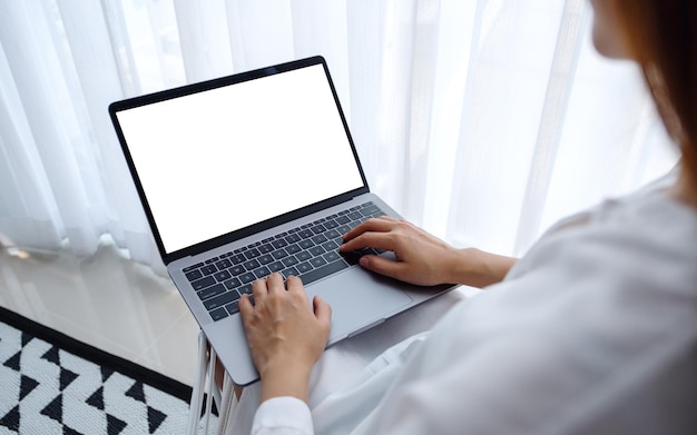 Mockup image of a woman working and typing on laptop computer with blank screen while sitting in a bedroom at home