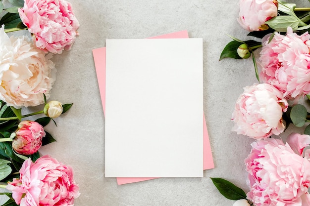 Photo mockup invitation blank paper greeting card pink envelope and peonies on gray stone table flower background flat lay top view