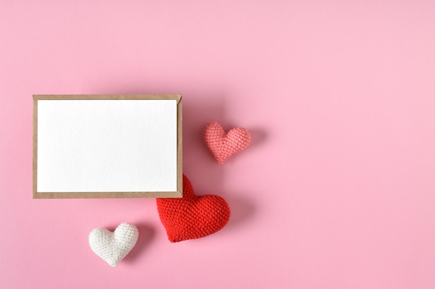 A mockup of a kraft envelope with a blank sheet and knitted hearts Valentine's Day greeting card with hearts on a pink background