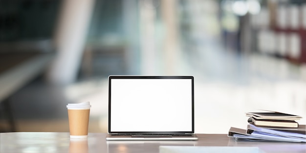 Mockup laptop computer, paper coffee cup, document file on business table with empty screen.