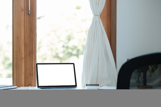 Mockup laptop with blank screen on white table with calculator and graph chart paperwork home