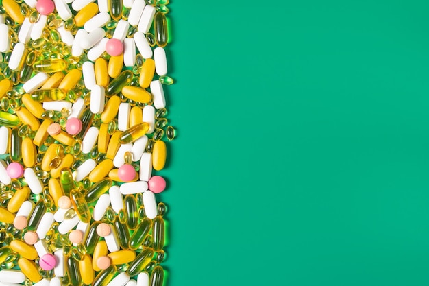 Mockup multicolored pills and yellow gel capsules on a green background space for text