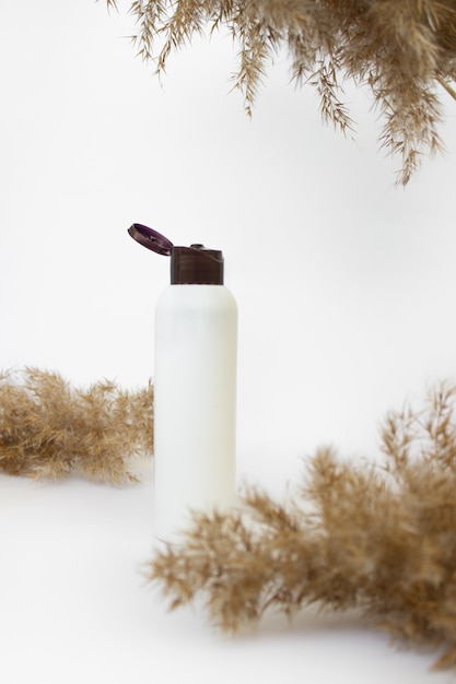 Mockup of a white cosmetic bottle on a white background with reed branches