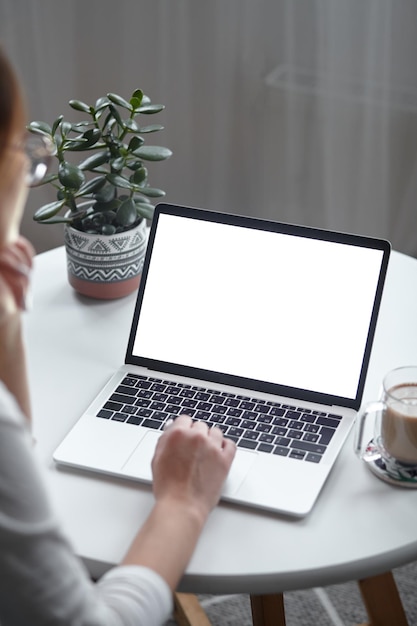 Mockup white screen laptop woman using computer while sitting at table at home back view