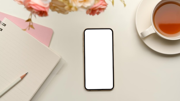 A mockup white screen of smartphone on minimal feminine white workspace with supplies top view