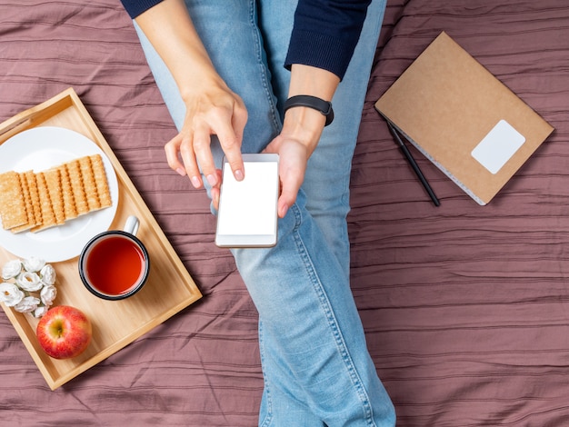 Mockup with woman with smartphone, touching the screen, home furnishings, bed, flat lay