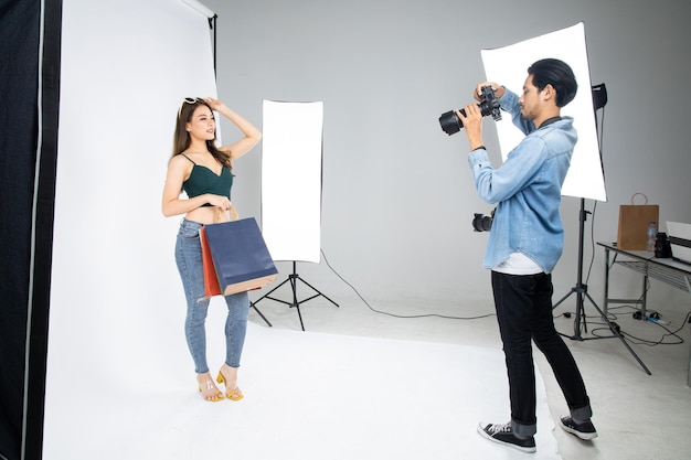 Model beautiful girl posing for a photo taken with a professional photographer in the studio in shopping concept. Photographer and model. Young man photographing fashion model.