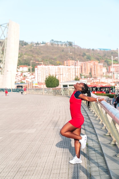 Model Black afro girl posing smiling and fun in the city at sunset wearing a red dress and white sneakers