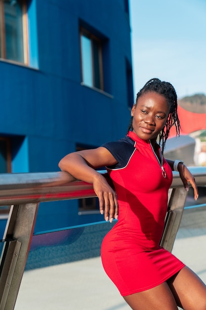 Model Black afro girl posing smiling and fun in the city at sunset wearing a red dress and white sneakers