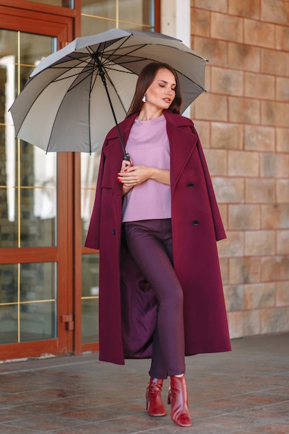 A model girl showing fashionable outerwear with an umbrella in her hand on the street on the veranda of a summer cafe Clothes for the showroom