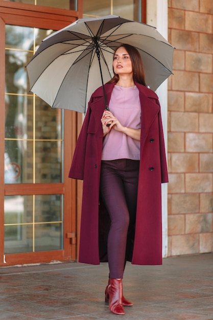 A model girl showing fashionable outerwear with an umbrella in her hand on the street on the veranda of a summer cafe Clothes for the showroom