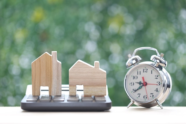 Model house on calculator and alarm clock on natural green background