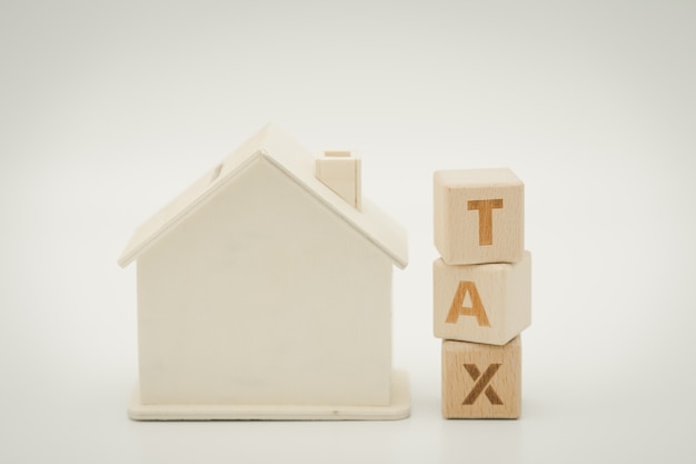 A model house model is placed on wood word TAX . as background property real estate 