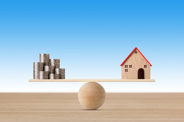 Model house on seesaw balancing with stacking coins money on blue background.