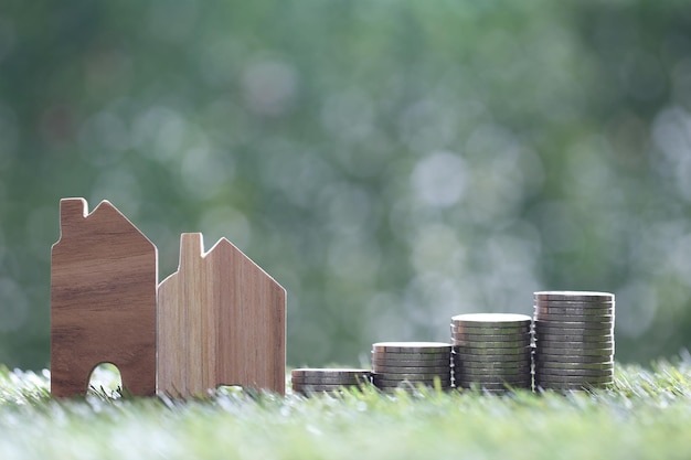 Model house and stack of coins money on natural green background