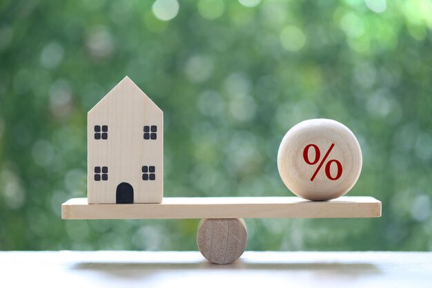 Model house with Percentage symbol icon on wood scale seesaw on natural green background