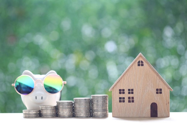 Model house with stack of coins money on natural green background