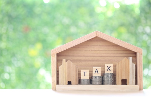 Model house with stack of coins money and tax word on green background