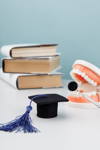 Model of jaw with dentist tool and graduation cap with books. Medical education concept. Vertical image.