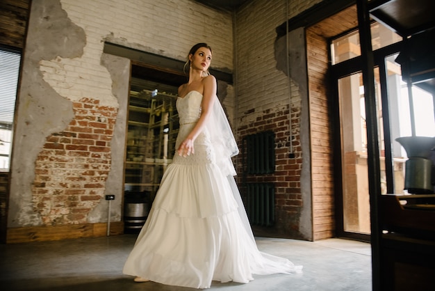 Model posing in a white long wedding dress indoors by the window. 