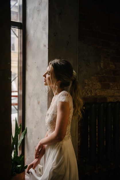 Model posing in a white long wedding dress indoors by the window