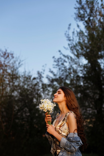 model in the sun on a walk in the summer. in the hands of a bouquet of flowers. blurred space. happiness and a smile on your face