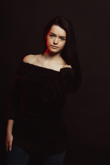 Model test with gorgeous brunette woman in knitted sweater posing over a black studio background