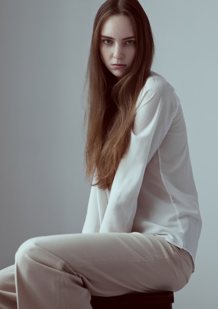 Model test with young beautiful fashion model with long hair wearing white shirt on grey background