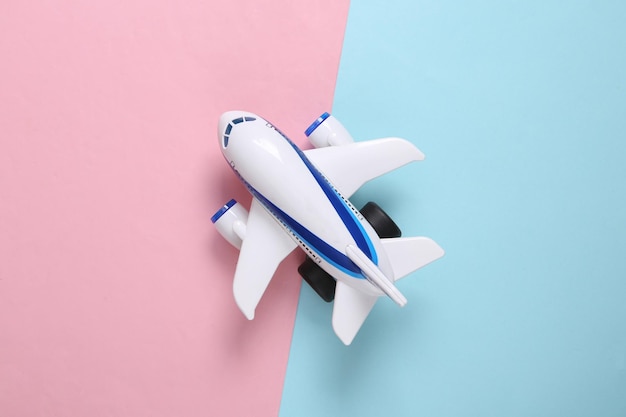 Model of a toy passenger plane on a bluepink pastel background Travel concept Top view