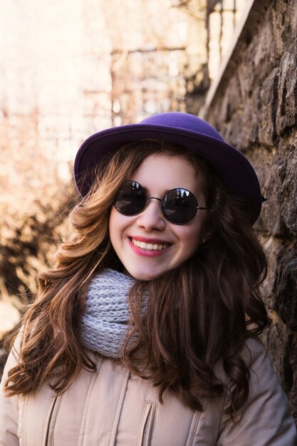 Model wearing sunglasses, scarf and jacket over a brick wall